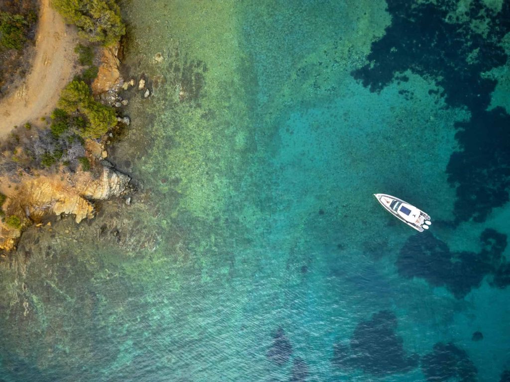 A top-down aerial view of the Saxdor 320 GTO 'Paralos' yacht anchored in the clear, turquoise waters of a serene cove in Halkidiki