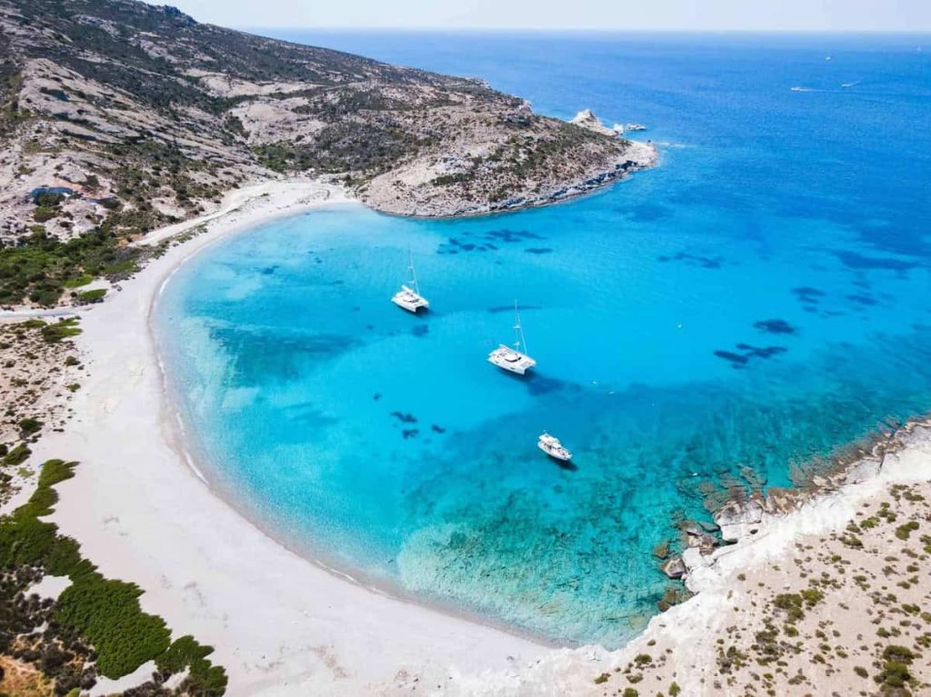 A stunning aerial view of a secluded bay in Halkidiki, showcasing three yachts anchored in the crystal-clear turquoise waters