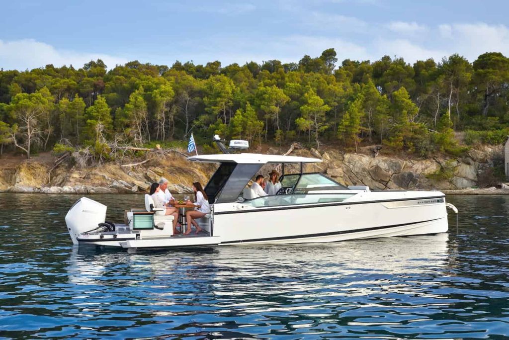 Luxurious Saxdor 320 GTO with guests on board, anchored near a lush, tree-covered shoreline