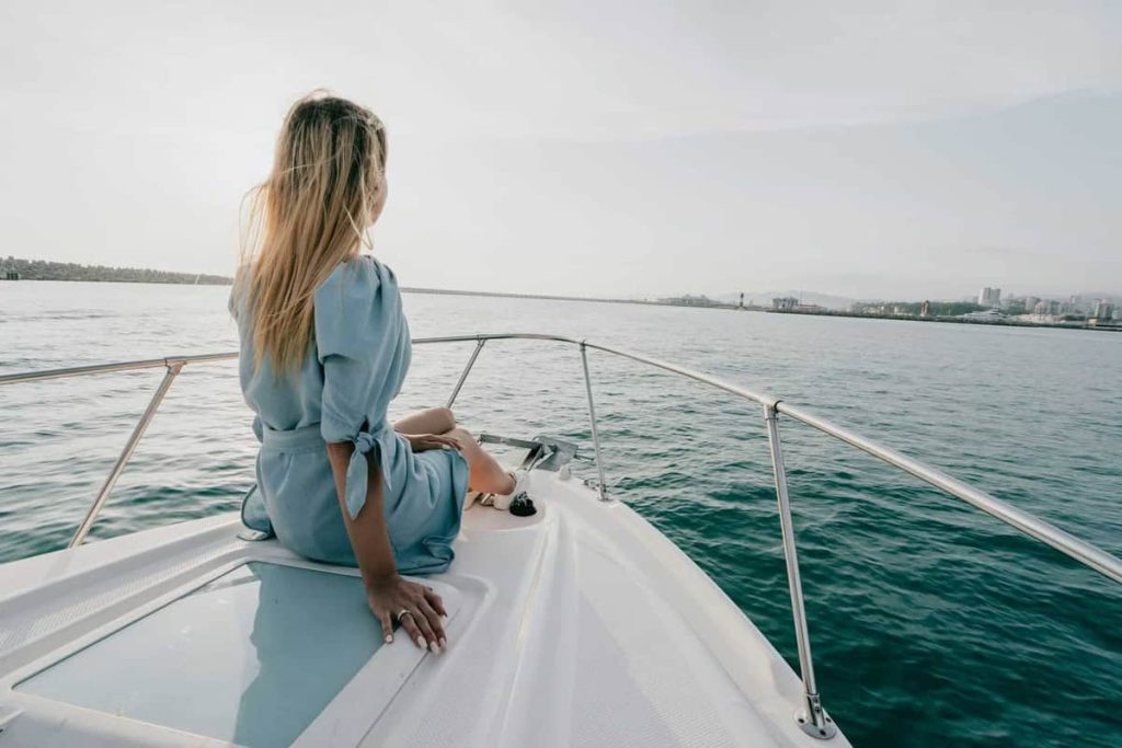 A woman in a light blue dress relaxes on the bow of a yacht