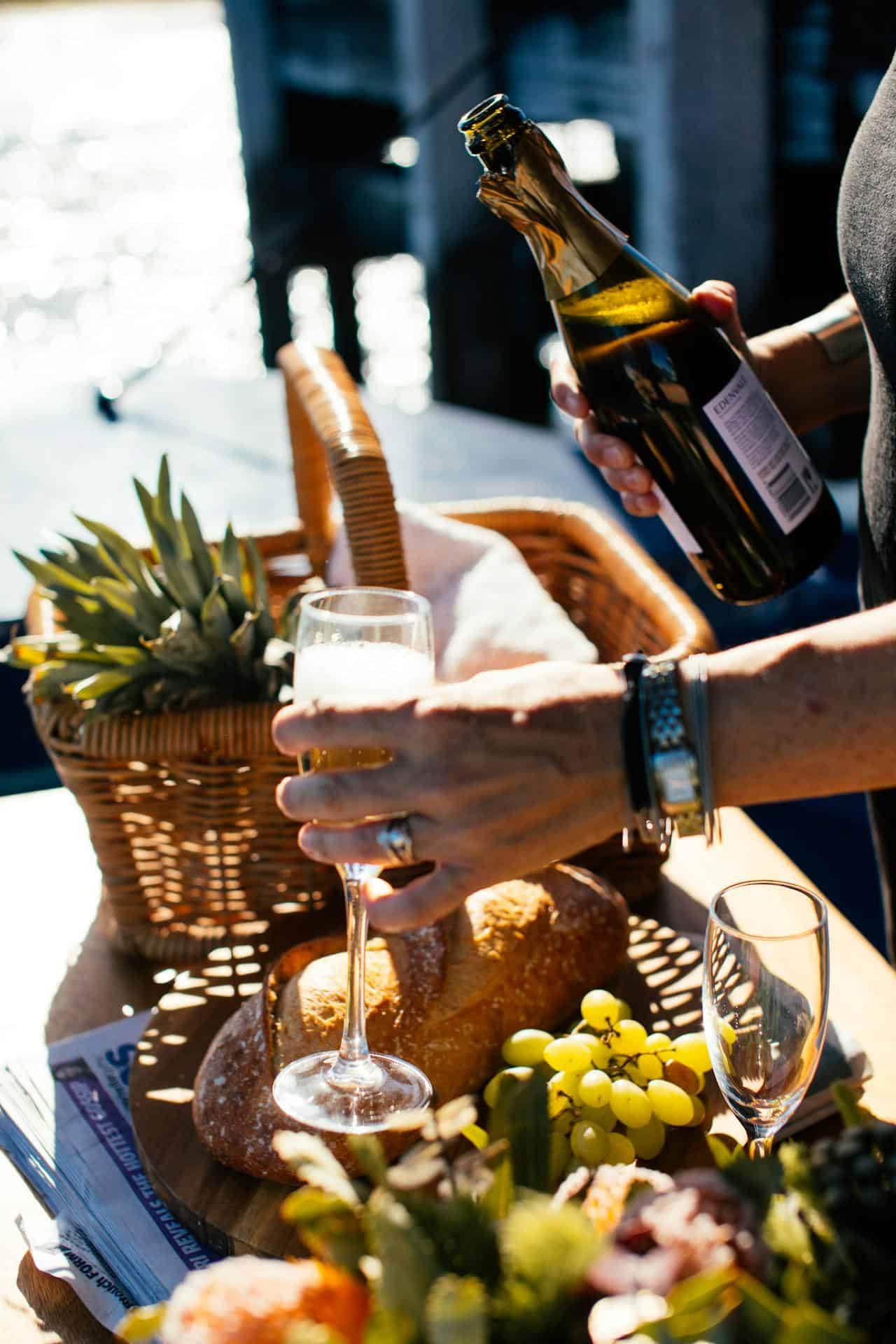 Close-up of a hand pouring champagne into a glass with a picnic basket on 'Paralos' yacht