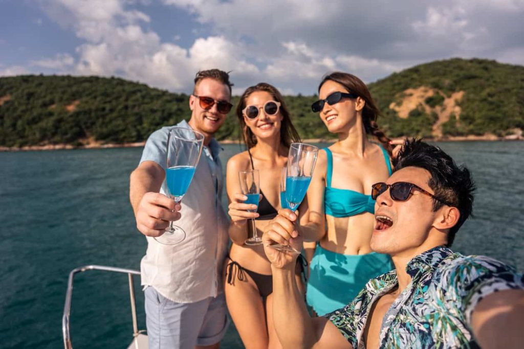 Group of friends raising glasses of blue cocktails on a yacht, celebrating and enjoying the beautiful sea views